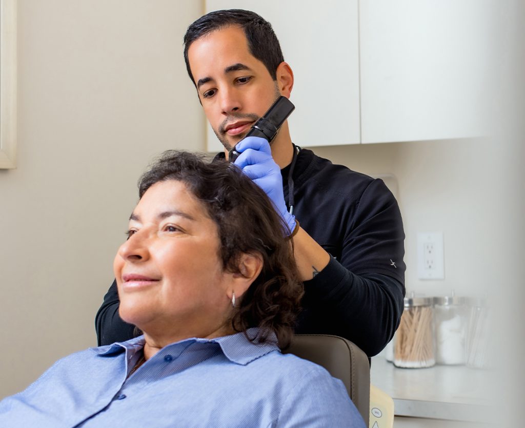 Clinician examining a woman's scalp while she sits in an exam chair.