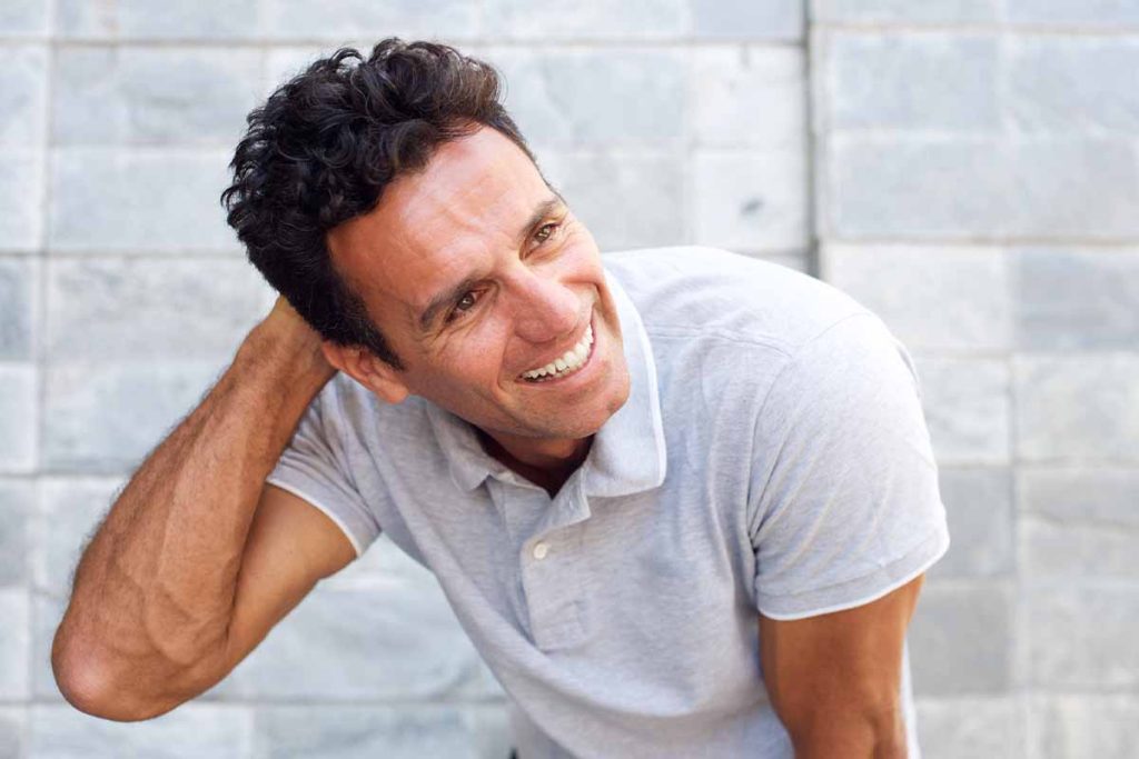 Smiling man with curly dark hair wearing a light gray polo shirt while looking to the side.