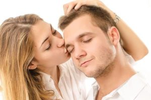 Woman kissing a smiling man on the cheek while gently holding his hair.