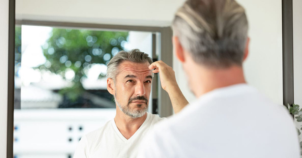 older man looking in the mirror after his artas robotic hair transplant in Miami, FL