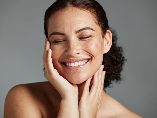 Smiling woman with her eyes closed resting her face in her hands.