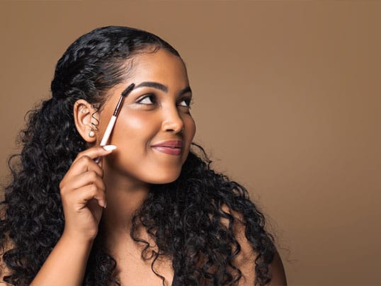 Woman using an eyebrow brush to groom and shape her eyebrows.