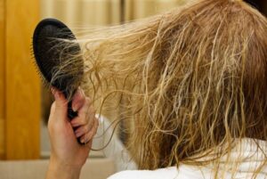Person brushing dry, tangled hair, illustrating damage from excessive hair styling.