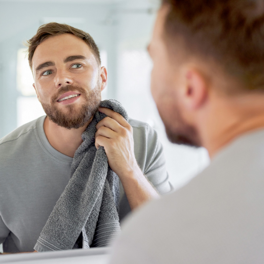 Man looking at his reflection while drying his jawline with a towel.
