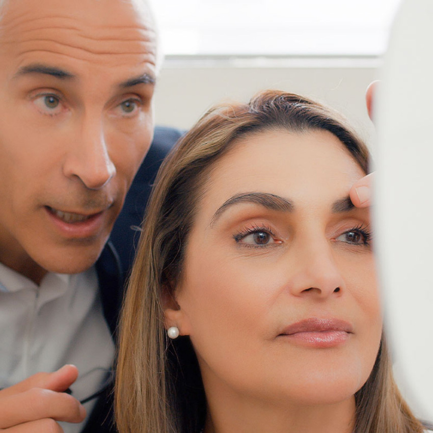 Dr. Jeffrey Epstein, Miami board-certified facial plastic surgeon, discussing facial anatomy with a patient during a consultation as the patient looks in a handheld mirror.