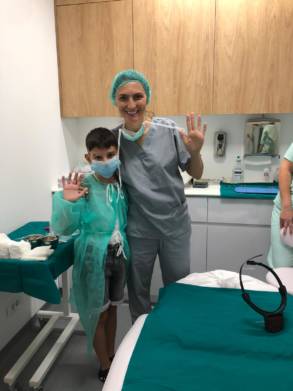 Young patient posing with the surgeon after a successful facial procedure in the treatment room.