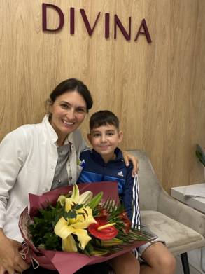 Surgeon posing with a smiling young patient holding a bouquet during a post-procedure follow-up visit.