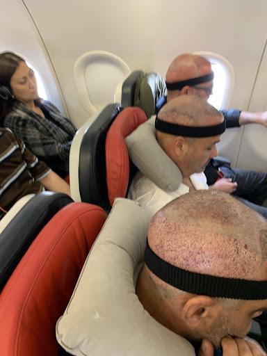 Passengers wearing headbands and neck pillows on a flight after hair transplant procedures.